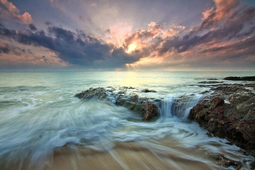 Beautiful sunrise over ocean rocks with waves crashing, capturing the serenity and power of nature.